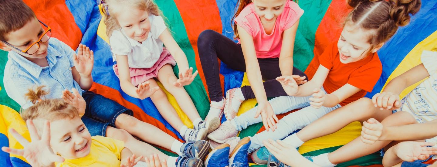 Kids sitting in a circle on a colourful parachute