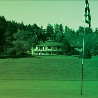 A golf green with a flag. A clubhouse is in the background